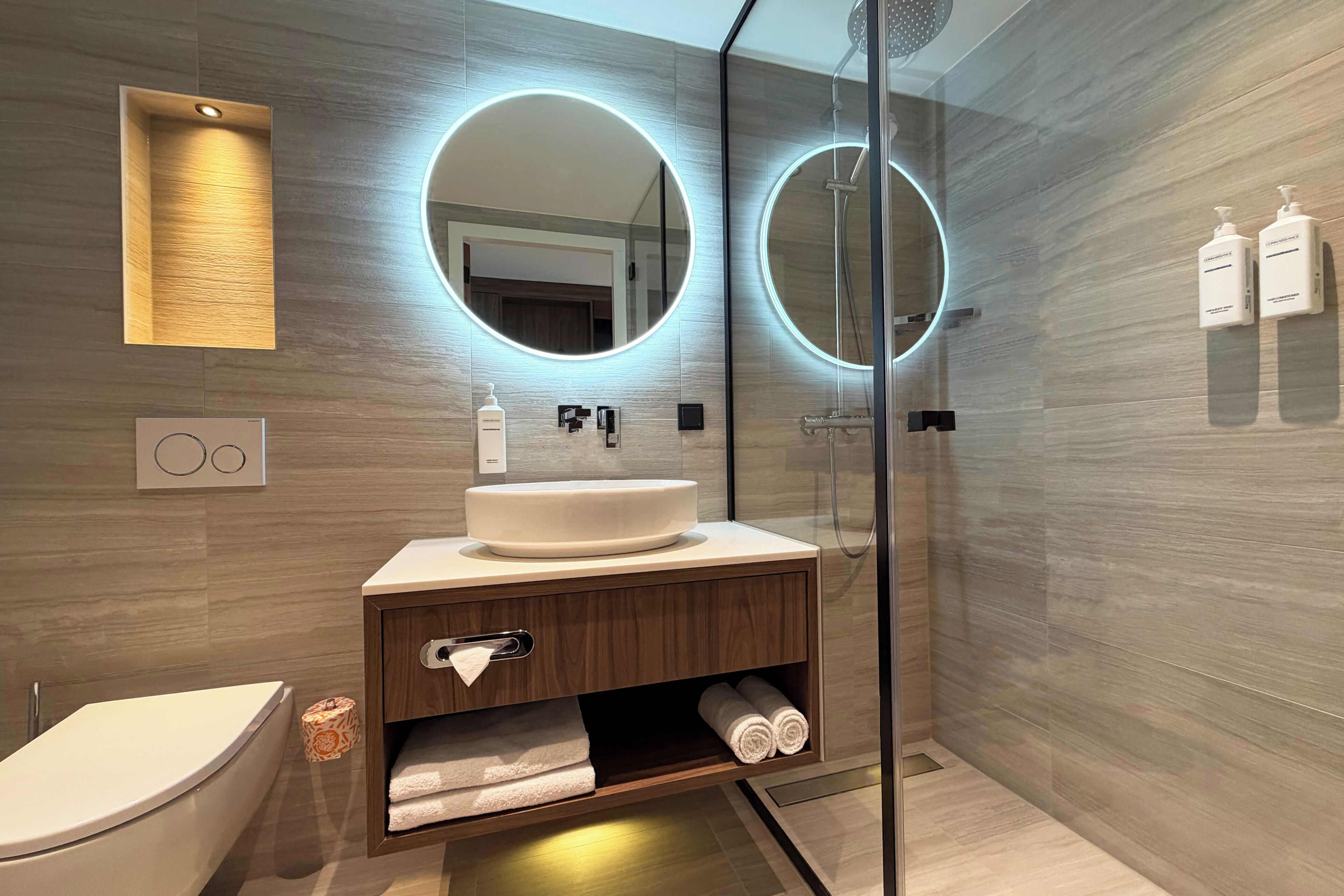 A modern bathroom with a round mirror, a toilet, a sink, and a shower.