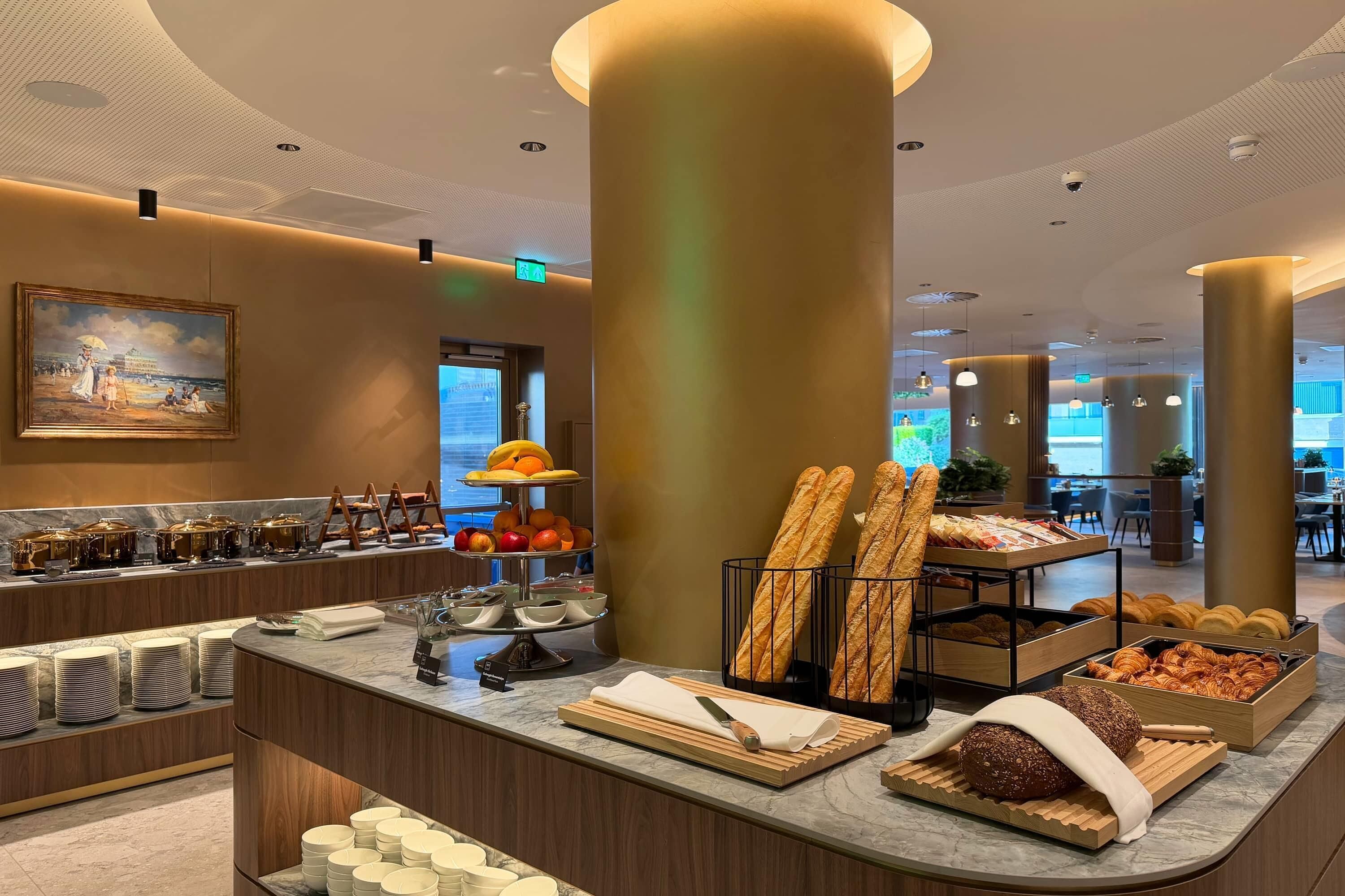 A hotel lobby with a buffet area featuring bread, pastries, and fruits.