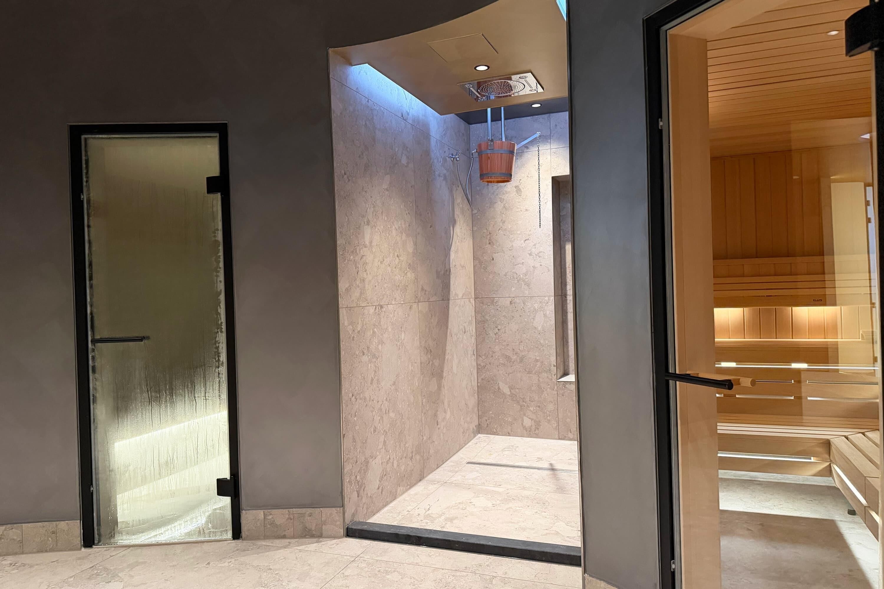 A modern interior with a glass door leading to a shower area with a wooden bucket and a tiled floor.