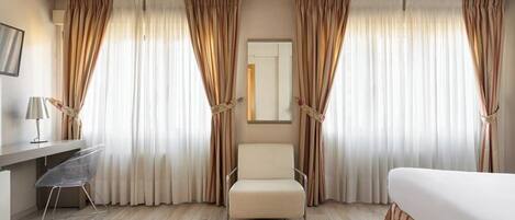 A hotel room with a bed, a desk with a chair, and curtains.