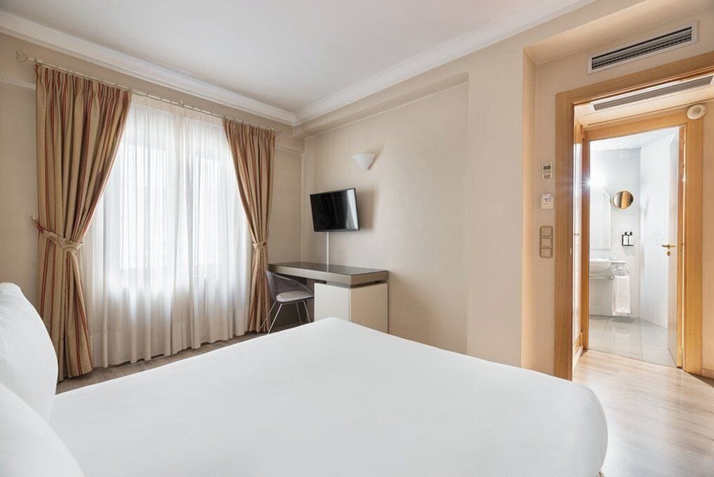 A hotel room with a large bed, a desk, a television, and a bathroom visible through an open door.