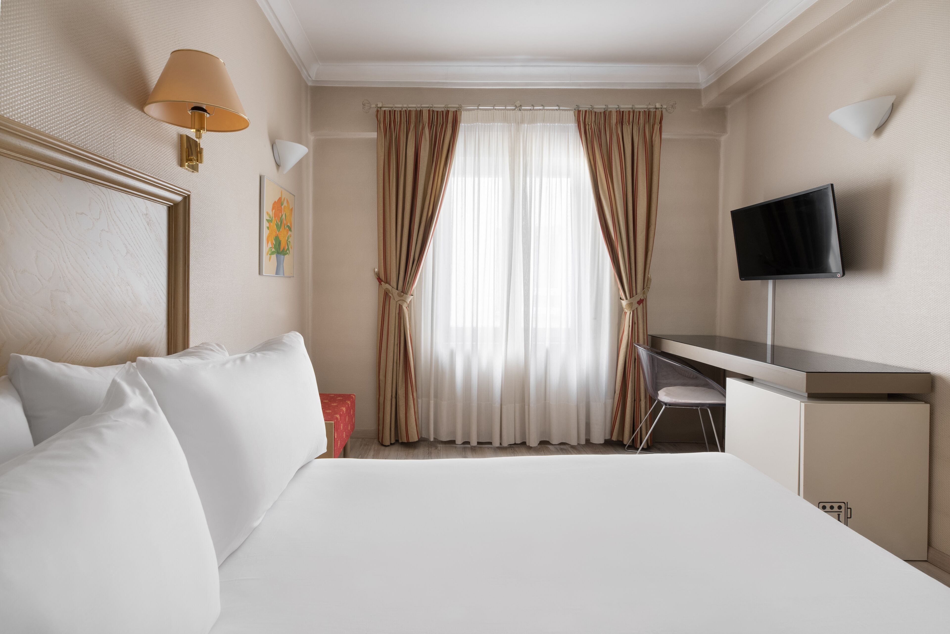 A hotel room with a bed, a desk, a chair, a TV, and curtains.