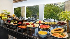 Un buffet proposant une variété de fruits et de plats, le tout mis en valeur par un décor verdoyant et de grandes fenêtres.