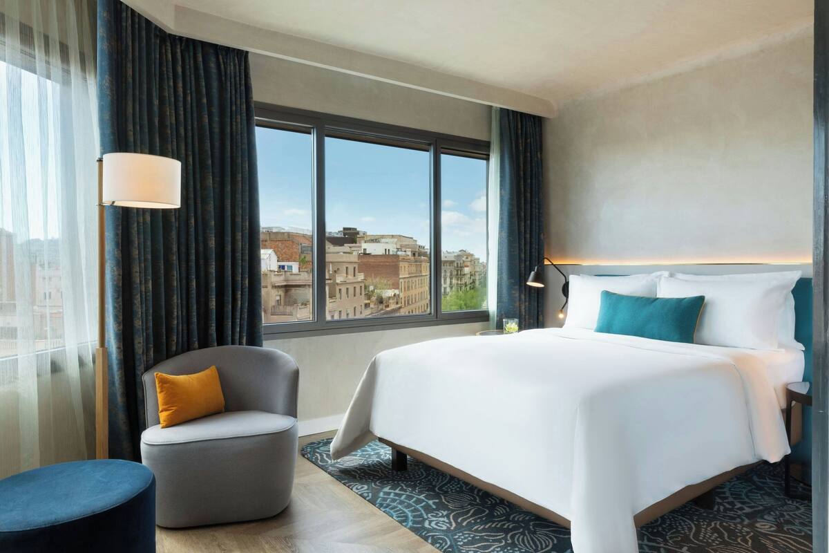 A hotel room with a large bed, a seating area, and a view of the cityscape through the window.
