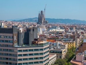 Un hôtel moderne doté d’une piscine sur le toit, entouré d’immeubles urbains et offrant une vue lointaine sur une cathédrale.