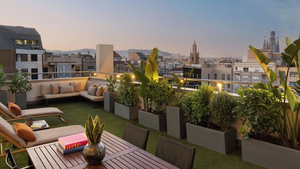 Une terrasse sur le toit, avec une table en bois, des chaises longues et des plantes en pot.