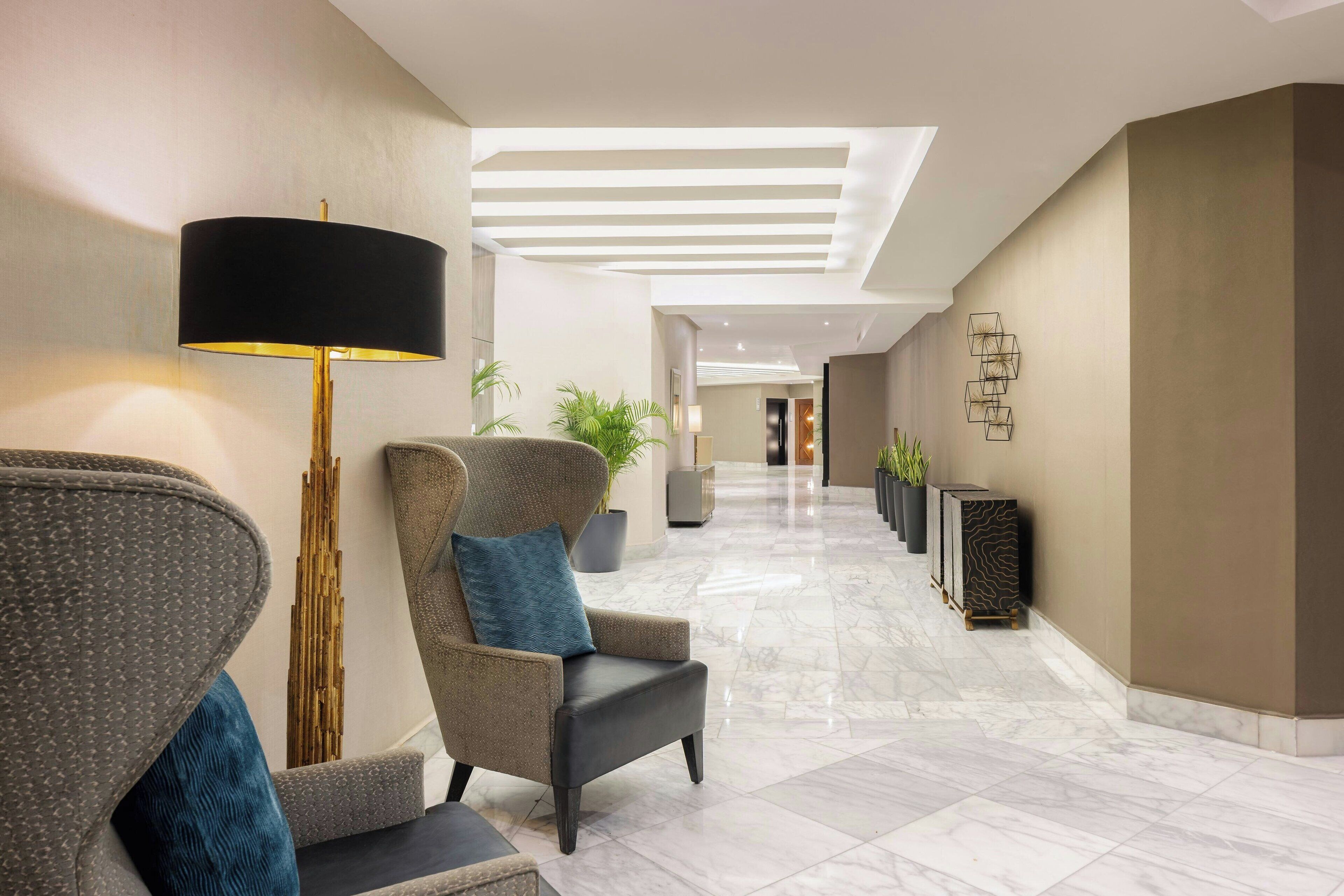 Un moderno vestíbulo de hotel con zona de estar, una lámpara de pie y un adorno geométrico en la pared.
