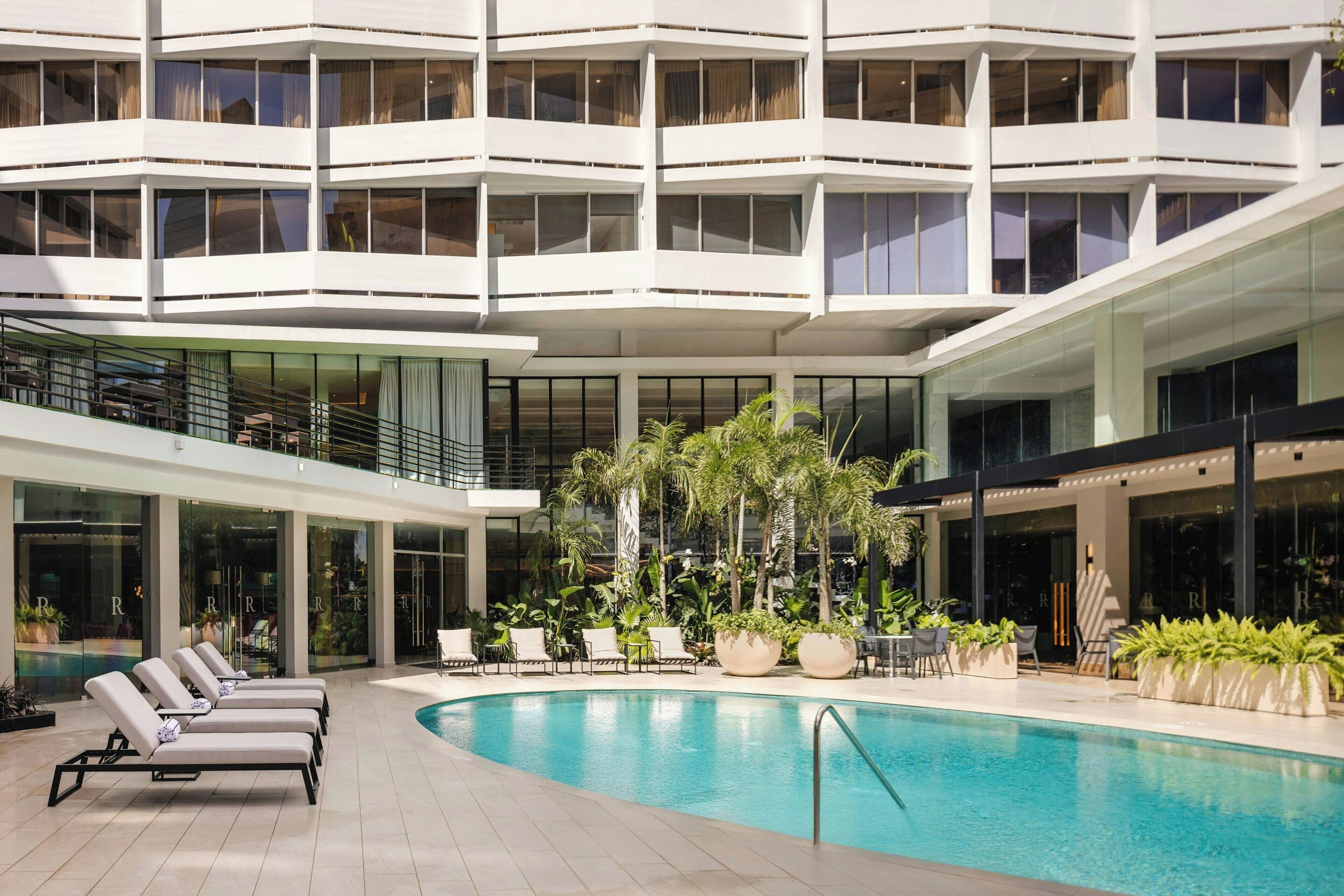 Un hotel moderno con una amplia piscina cubierta, varias zonas de descanso y una terraza en la azotea.