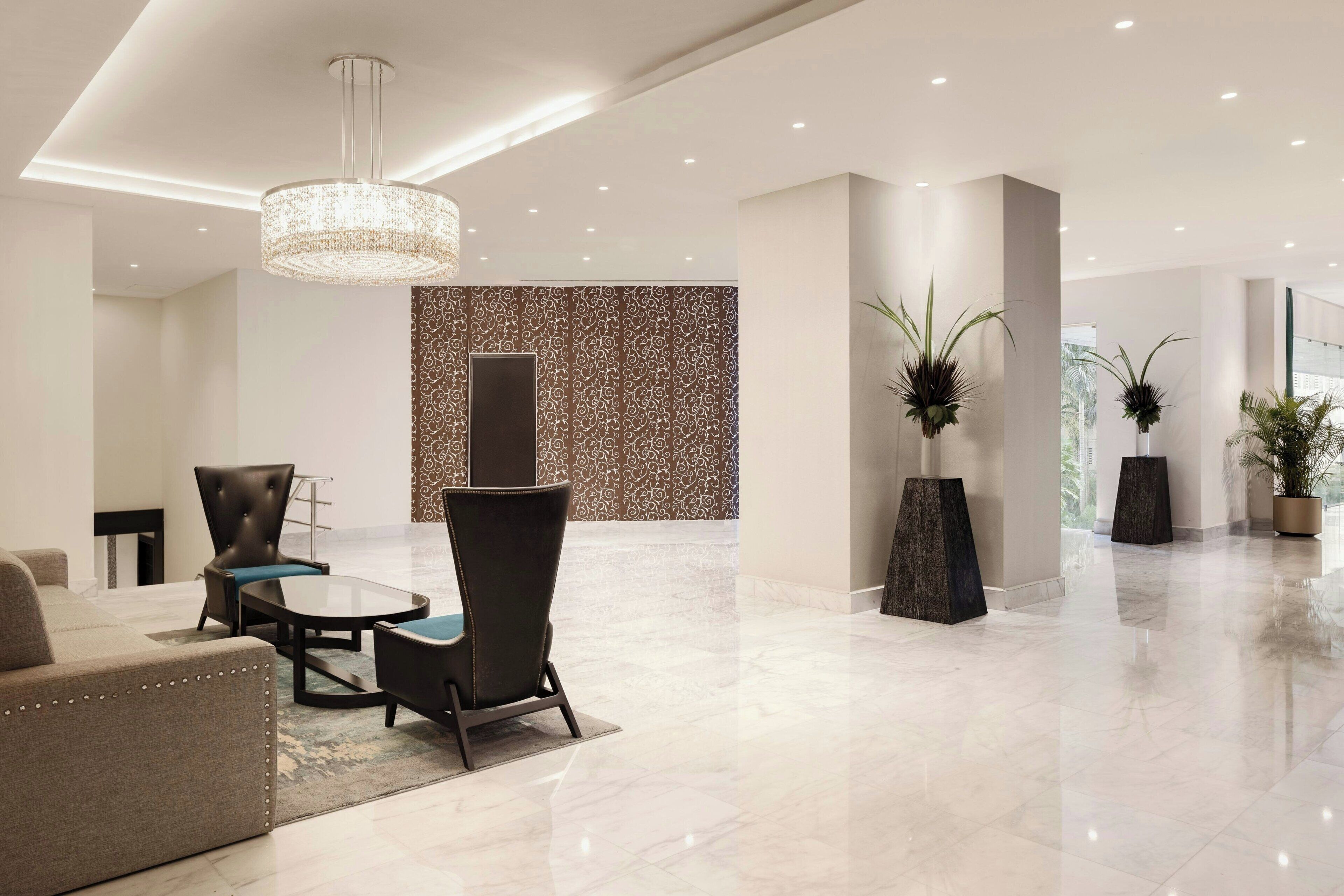 A modern lobby with a chandelier, seating area, and decorative plants.