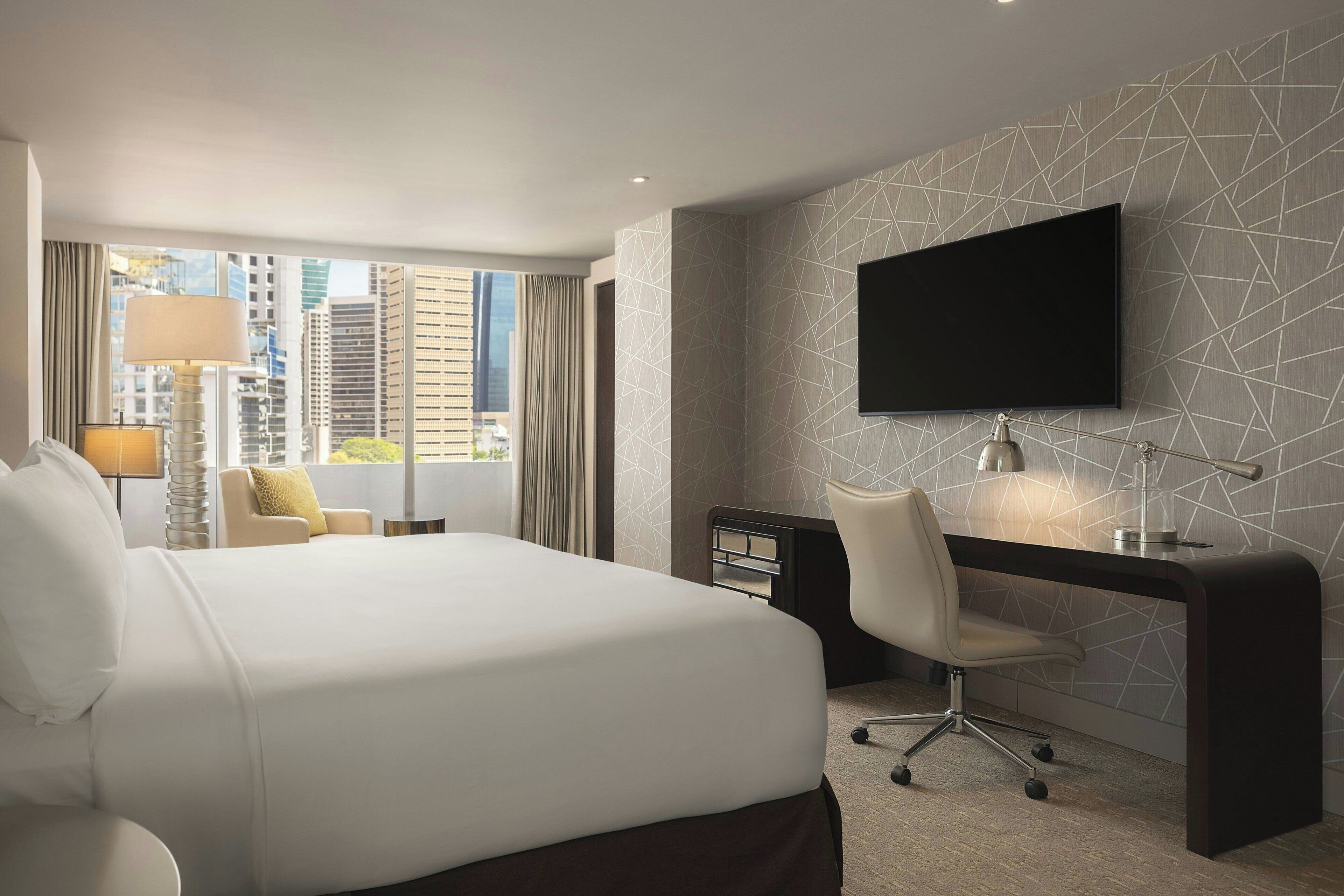 Une chambre d’hôtel avec un grand lit, un bureau, une chaise, une télévision et une vue sur le paysage urbain.