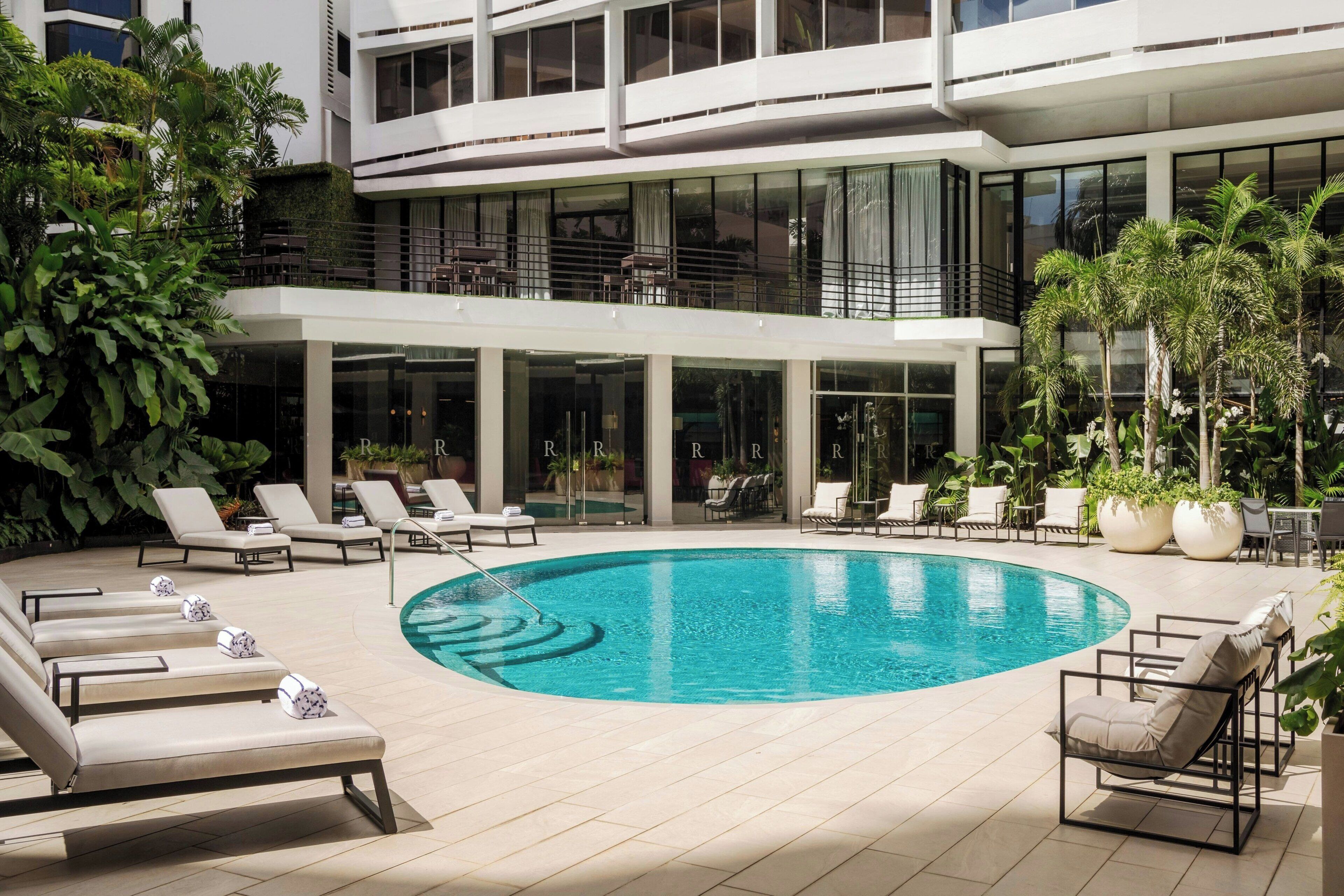 Un hotel moderno con piscina en la azotea, sillas de descanso y plantas en macetas.