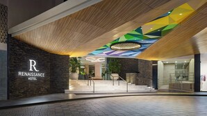 Exterior del Hotel Renaissance con un diseño moderno, que presenta un llamativo logo en forma de 'R', un diseño geométrico en el techo y un área de entrada bien iluminada.
