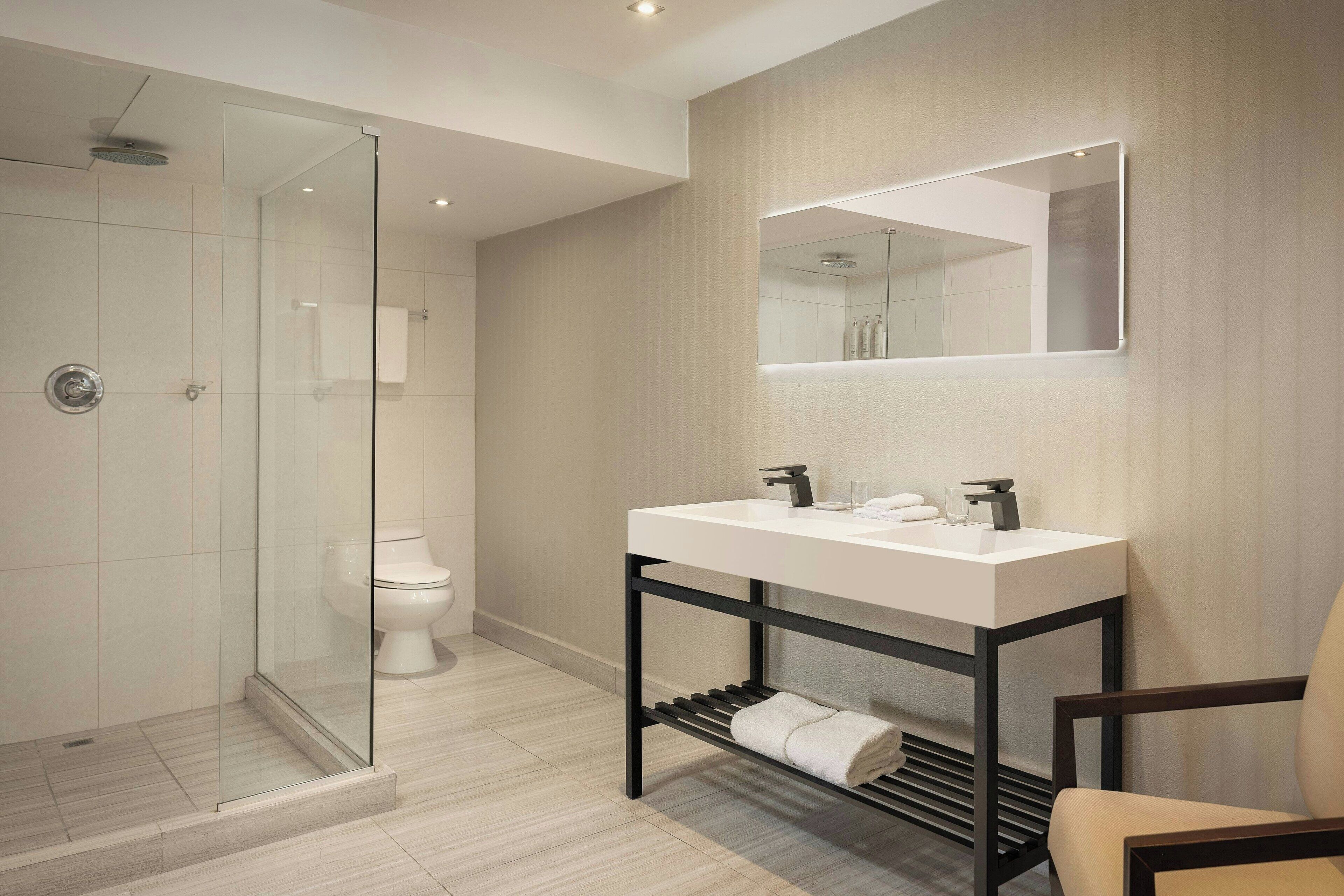 A modern bathroom with a glass-enclosed shower, a white sink with a black frame, and a large mirror above the sink.