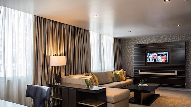 Una habitación de hotel moderna con un sofá, una mesa de centro, un televisor montado en la pared y un comedor con mesa y sillas.