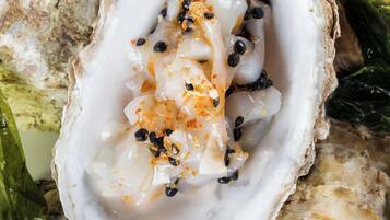 An oyster with a creamy sauce and black peppercorns on a bed of greens.