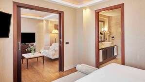 Habitación de hotel con cama, escritorio con silla, televisión, baño con lavamanos y espejo, y un espejo grande.
