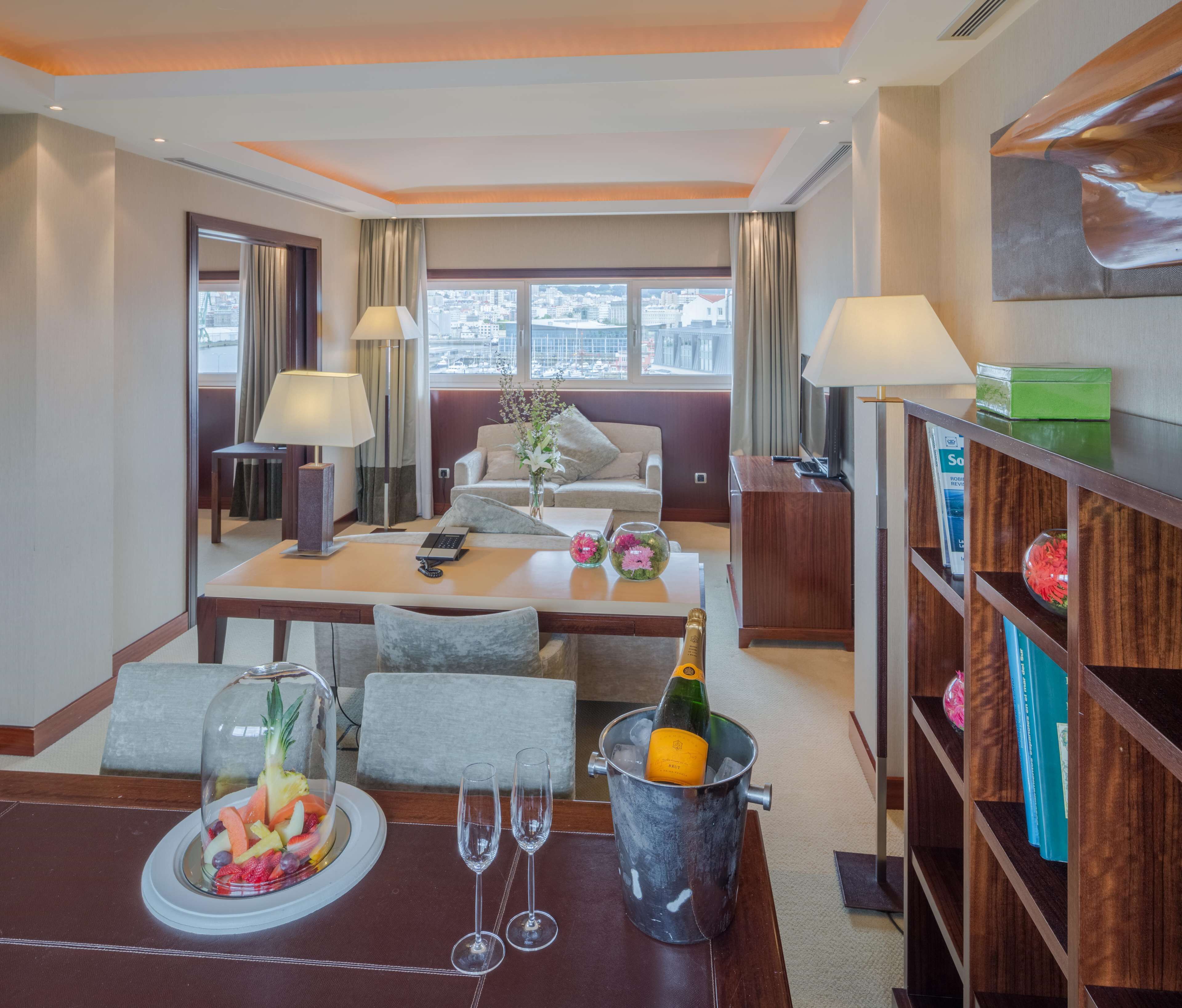 Habitación de hotel con comedor, sofá, escritorio con ordenador, minibar y vistas a la ciudad.