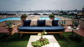 Área de piscina en la azotea con un sofá y una mesa, rodeada de sillones de descanso y plantas en macetas.