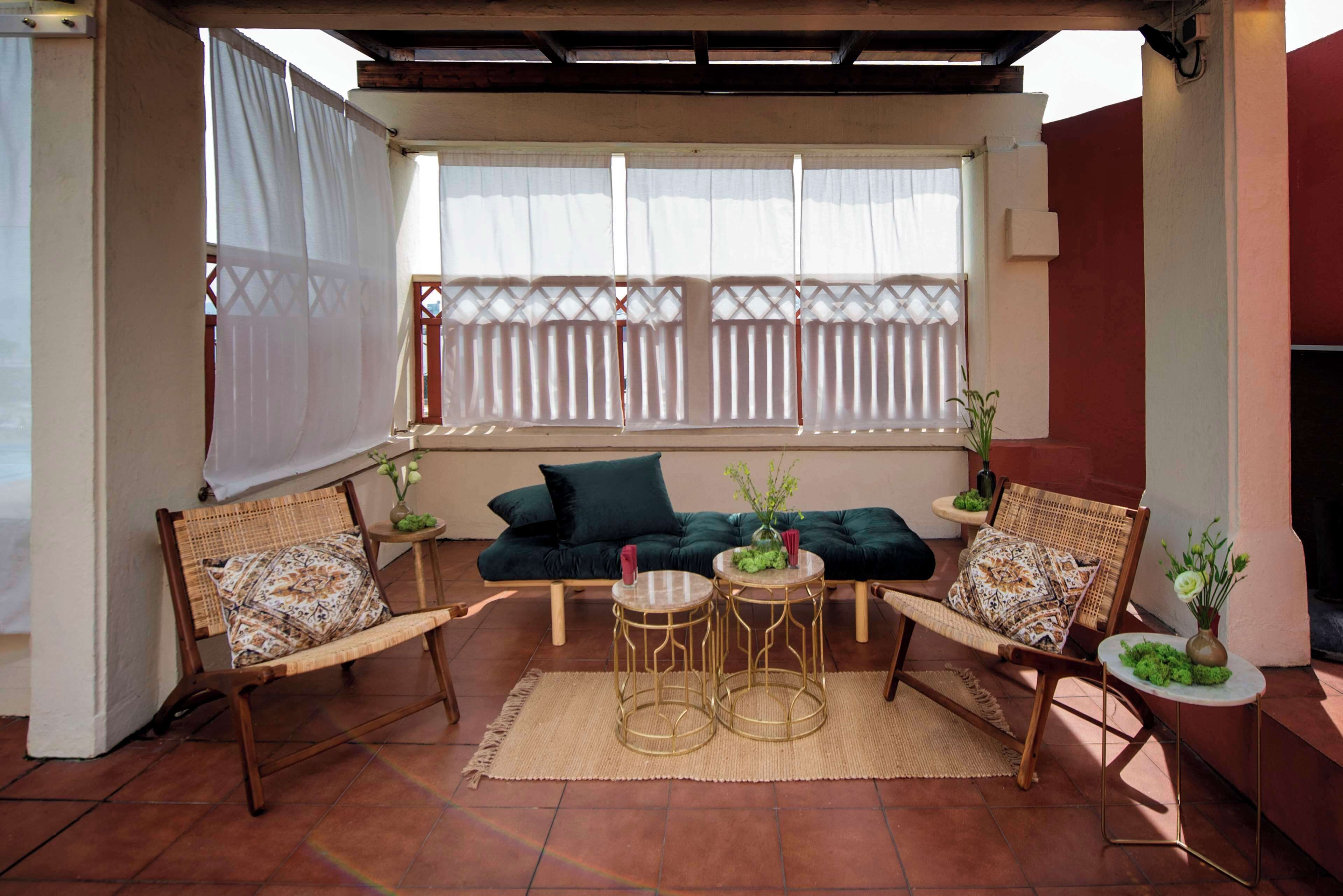 A covered patio area with a sofa, two chairs, and two round tables.