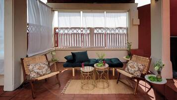 A covered patio area with a sofa, two chairs, and two round tables.