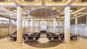 Un salón imponente con un escenario central, techo ornamentado y suelo de mármol.