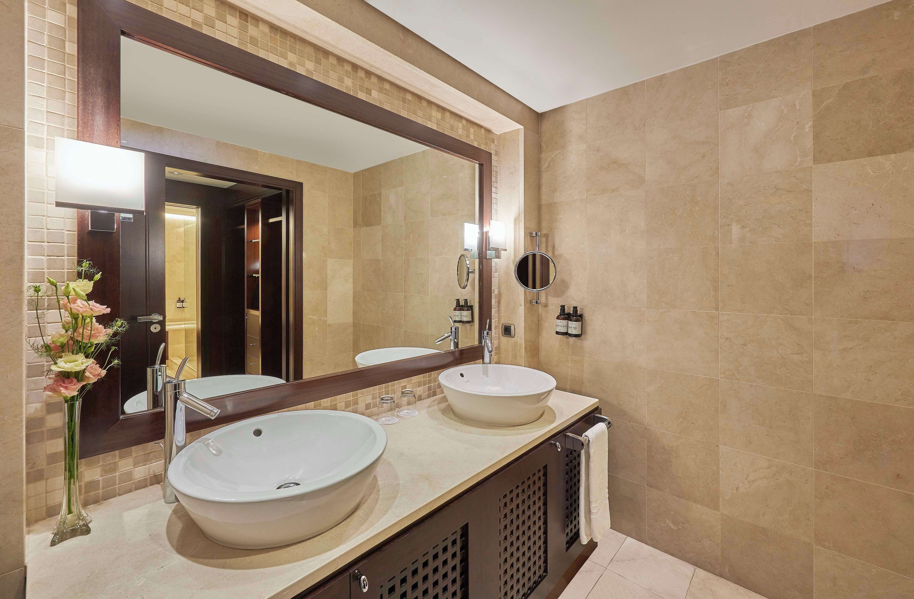 A bathroom with two sinks, a large mirror, and a vase of flowers.