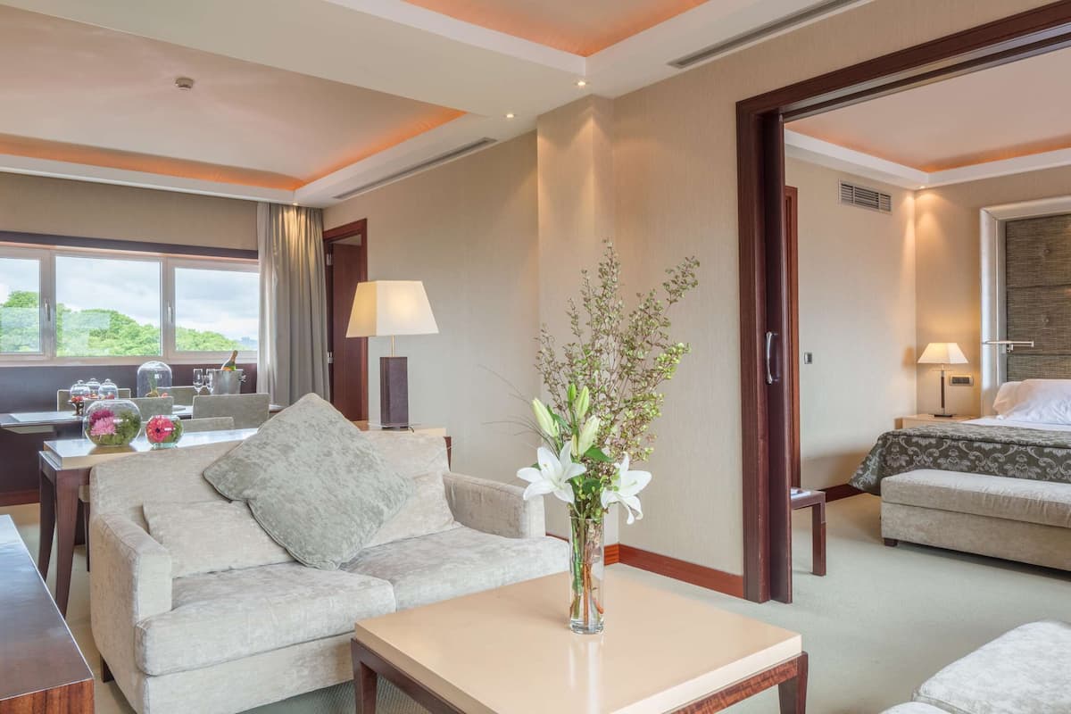 Habitación de hotel con sofá, una mesita de centro, un florero con flores, cama y vista a espacios verdes.