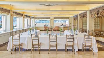 A banquet hall with a long table set for a formal event, flanked by chairs and adorned with floral centerpieces.
