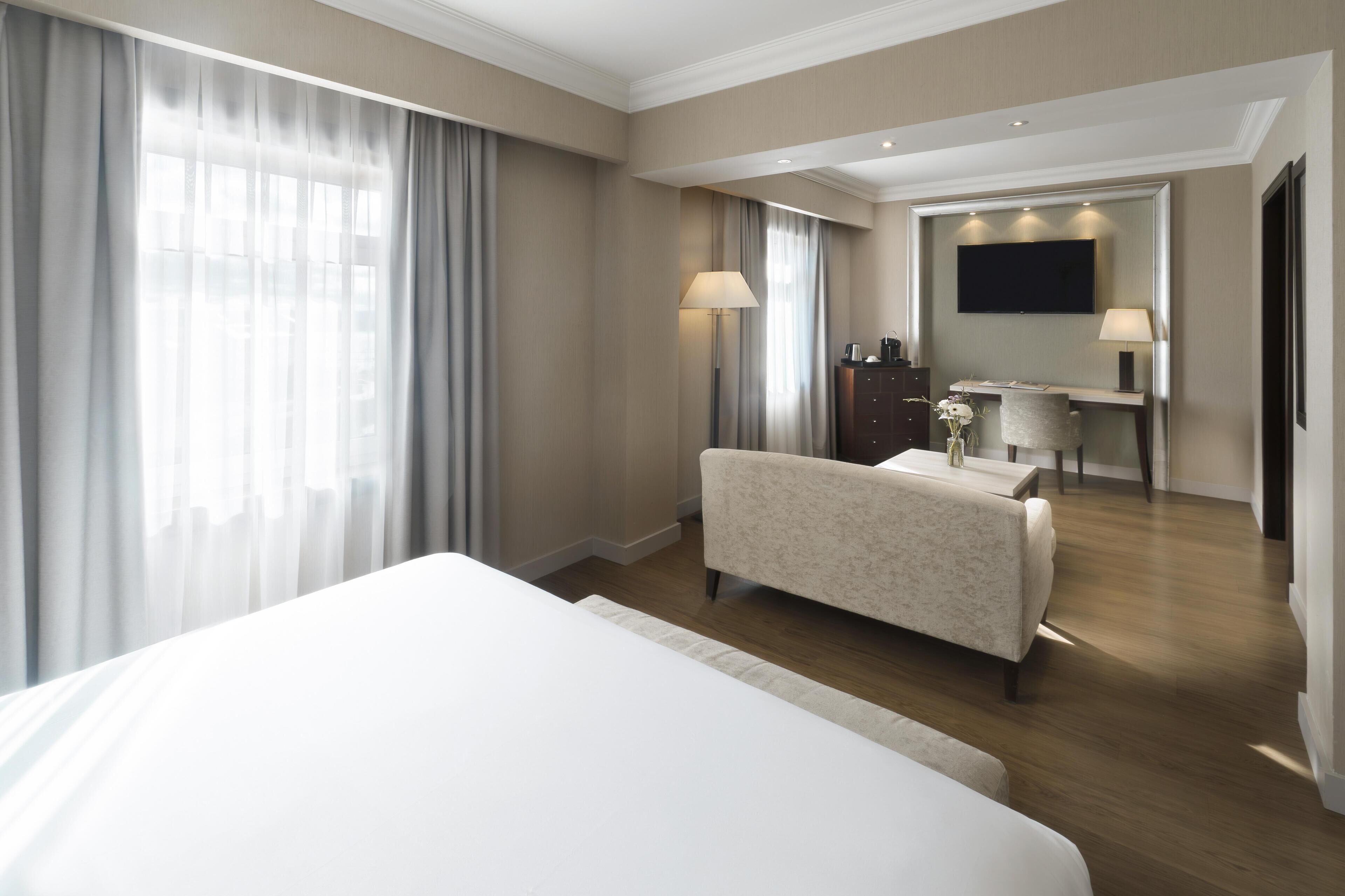 A hotel room with a large bed, a desk with a chair, a flat-screen TV, and a wardrobe.