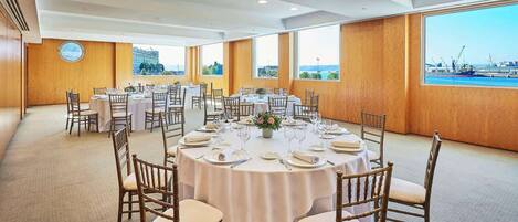 Un salón de conferencias con mesas redondas, manteles blancos y sillas de madera.