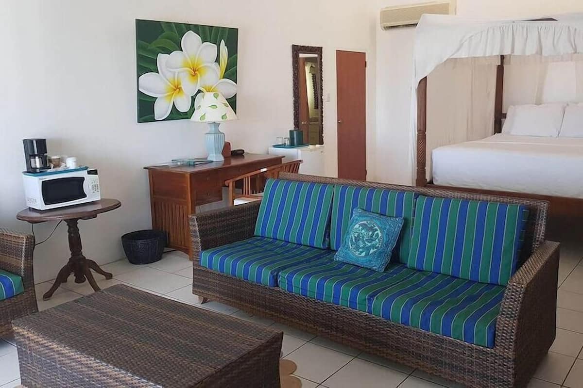 A room with a bed, a sofa, a dining table, a microwave, and a large flower painting.