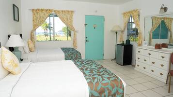 A bedroom with two beds, a door, a dresser, a lamp, and a window with curtains.