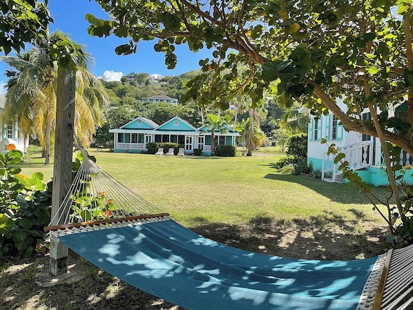 Una hamaca en un área verde con vista a una casa de techo azul y detalles blancos.