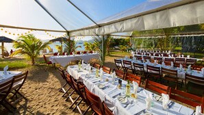 An outdoor dining area with tables set for guests, surrounded by palm trees and a view of the ocean. - Oualie Beach Resort (Newcastle)