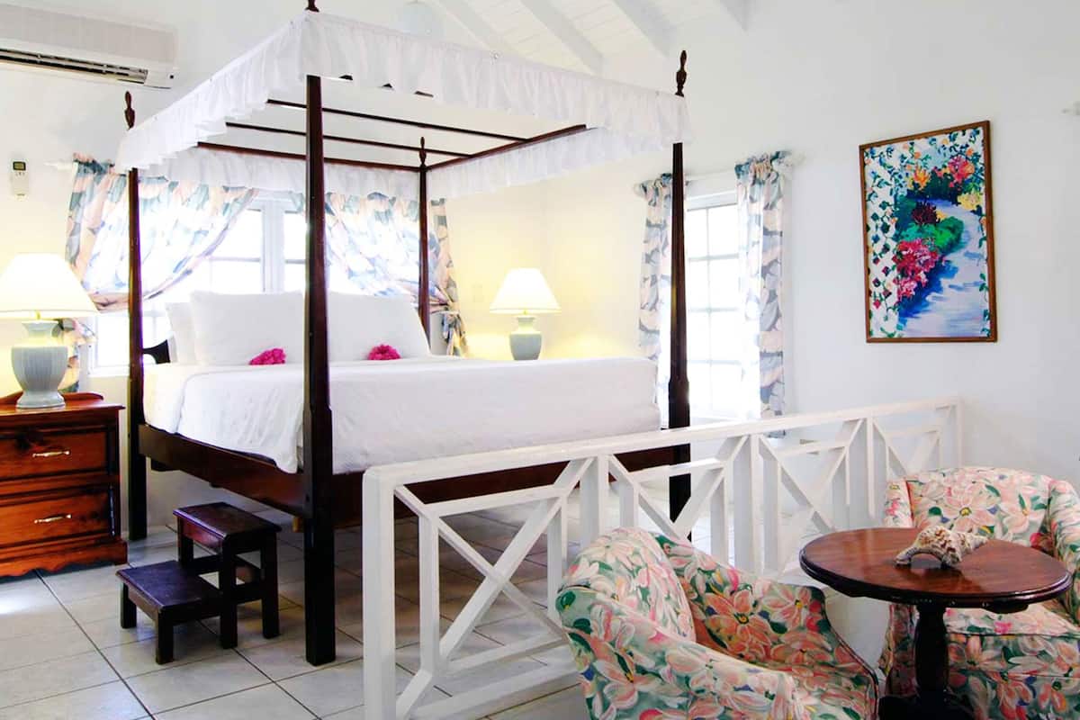 A four-poster canopy bed with white bedding, a wooden nightstand, a small table with a chair, and floral curtains.