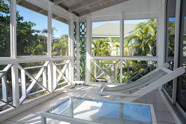 A sunlit room with a glass-enclosed pool, white railings, and a view of palm trees. - Oualie Beach Resort (Newcastle)