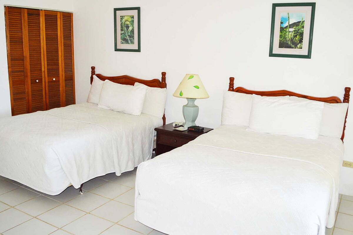 A double room with two beds, a wooden wardrobe, a nightstand with a lamp, and two framed pictures on the wall.