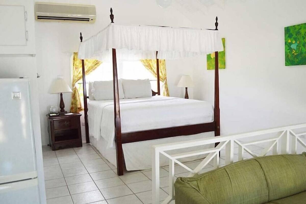 A four-poster bed with a canopy, a television, a green sofa, and a white-framed table.