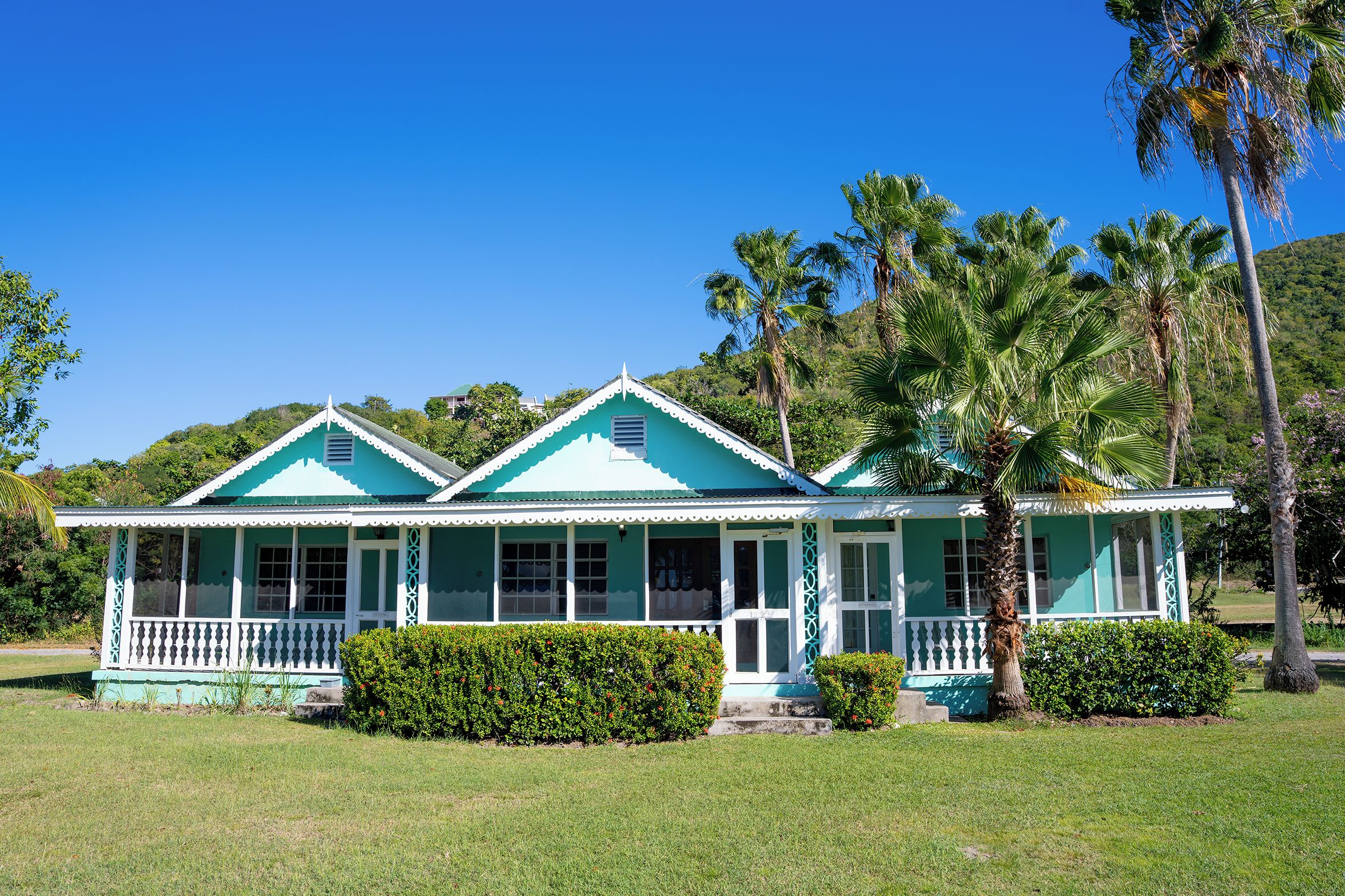 A two-story house with a porch, surrounded by well-maintained lawns and palm trees.