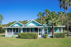 Een tweelaags huis met een veranda, omgeven door verzorgde gazons en palmbomen.