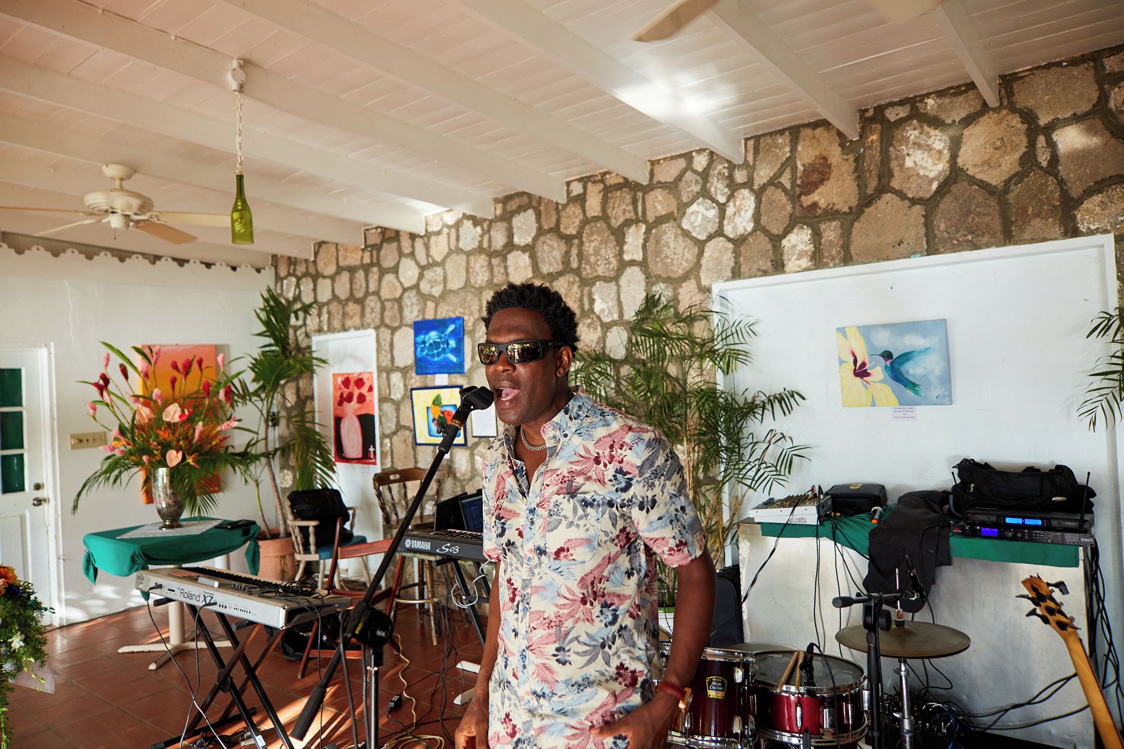 A person standing in a room with musical equipment, a stone wall, and artwork on the wall.