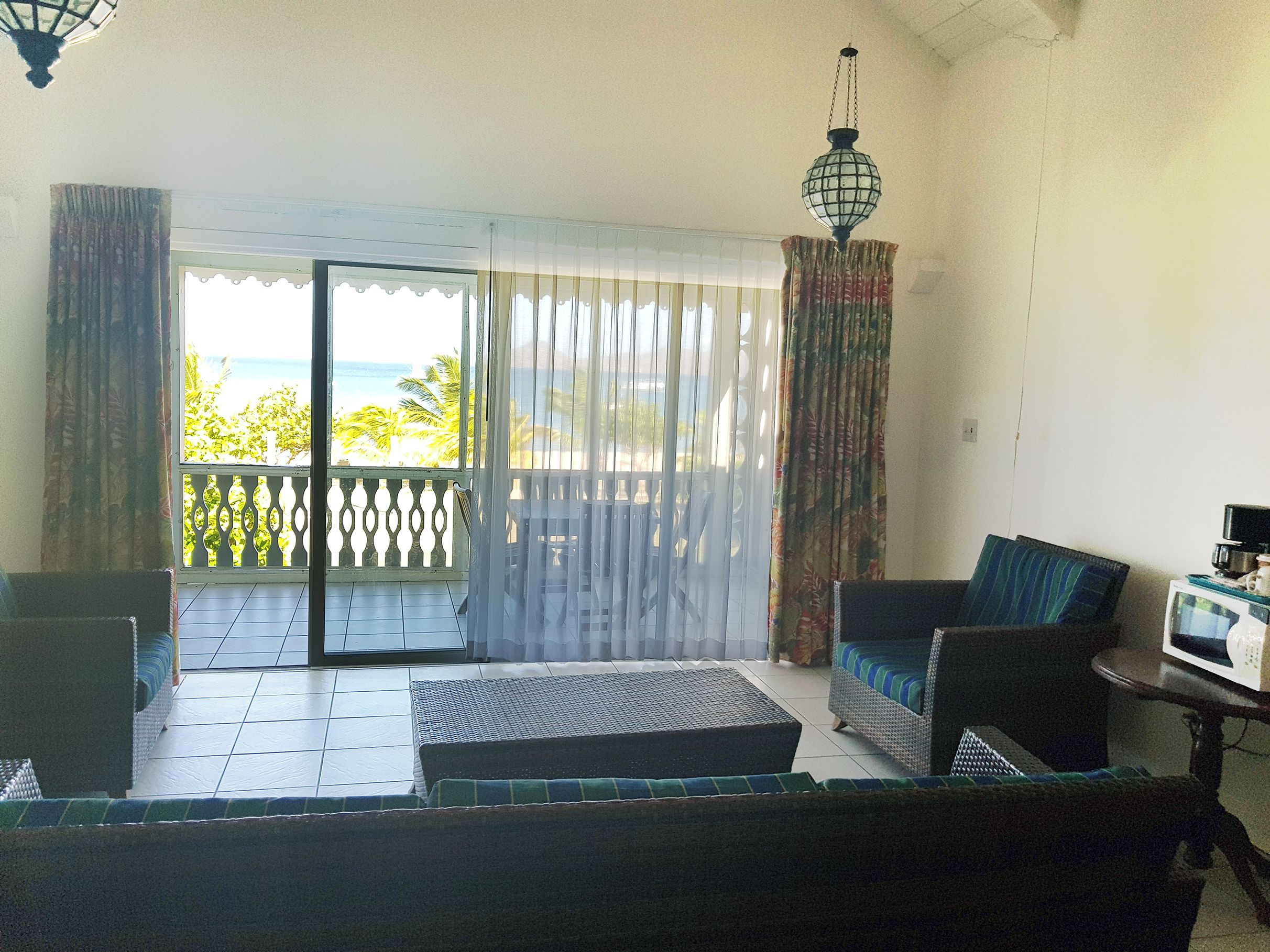 Uma varanda com vista para o mar, um sofá de vime, uma mesa pequena com micro-ondas e um lustre.