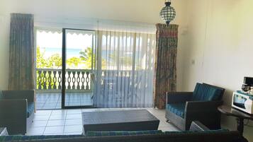 Uma varanda com vista para o mar, um sofá de vime, uma mesa pequena com micro-ondas e um lustre.