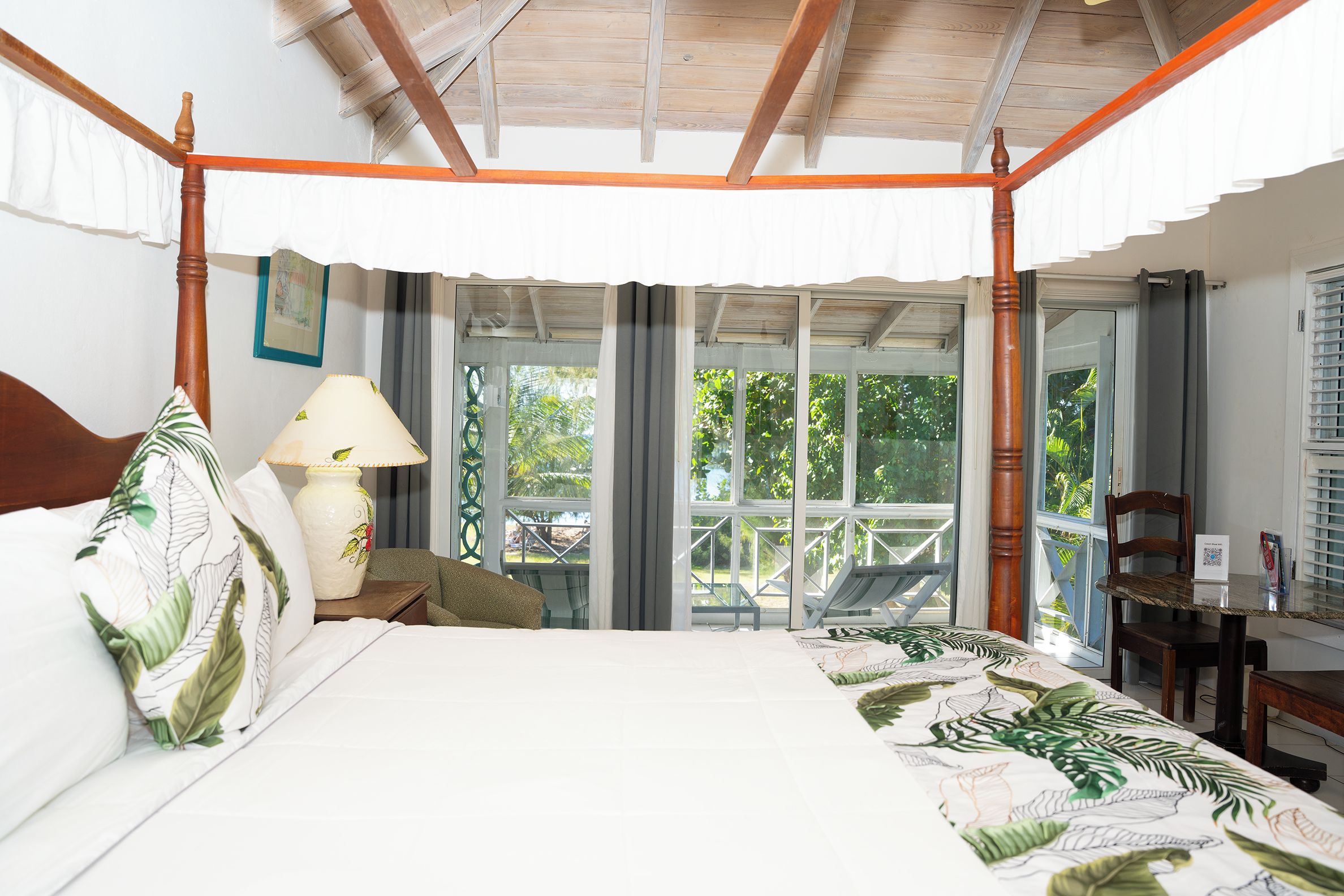 Una cama con dosel que ofrece vista a un balcón, una mesa con una lámpara y una silla.