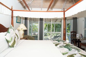 A four-poster bed with a view of a balcony, a table with a lamp, and a chair. - Oualie Beach Resort (Newcastle)
