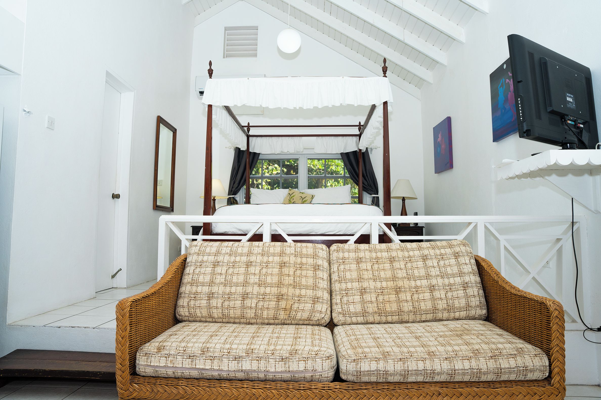 A room with a four-poster bed, a wicker sofa, and a television mounted on the wall.