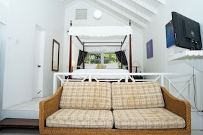 A room with a four-poster bed, a wicker sofa, and a television mounted on the wall. - Oualie Beach Resort (Newcastle)