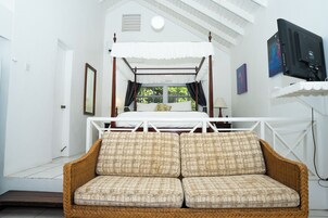 Um quarto com uma cama de dossel, um sofá de vime e uma televisão na parede.