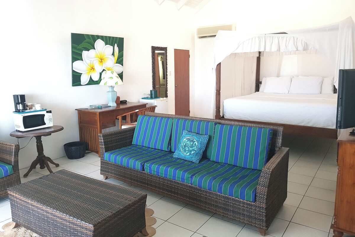 A room with a bed, a sofa, a small table with a microwave, a chair, and a painting on the wall.