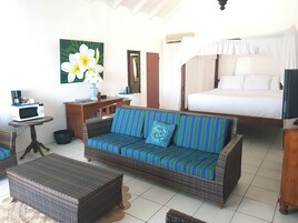 A room with a bed, a sofa, a small table with a microwave, a chair, and a painting on the wall.